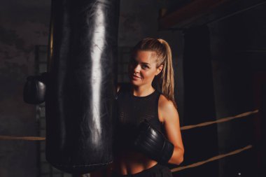 Güzel bayan boksör ringde duruyor eski bir spor salonunun kum torbasında, elleri boks eldivenlerinde. Kutu eğitiminde bir kadın. Sağlıklı yaşam tarzı, spor ve spor anlayışı. Boşluğu kopyala