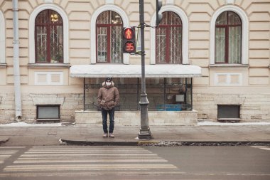 Gözlüklü, maskeli ve günlük kışlık kıyafetlerle şehirde yol geçen genç adamın portresi. Çekici bir genç soğuk ve bulutlu bir günde eski bir kasabada dikiliyor. Boşluğu kopyala