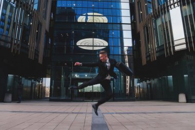 Düşünceli, çantalı genç bir işadamı şirket binasından ayrılıp sıçrama yapıyor, yaşam tarzı. Finans bölgesindeki ofisten ayrılan erkek bankacı