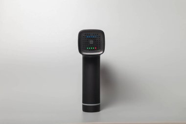 Gri arka planda, el bilgisayarı, profesyonel terapötik şok masaj silahı. Sporcular için derin kas dokularının perküsyon masajcısı, rahatlar, acıyı azaltır. Konsept spor ve sağlıklı yaşam tarzı