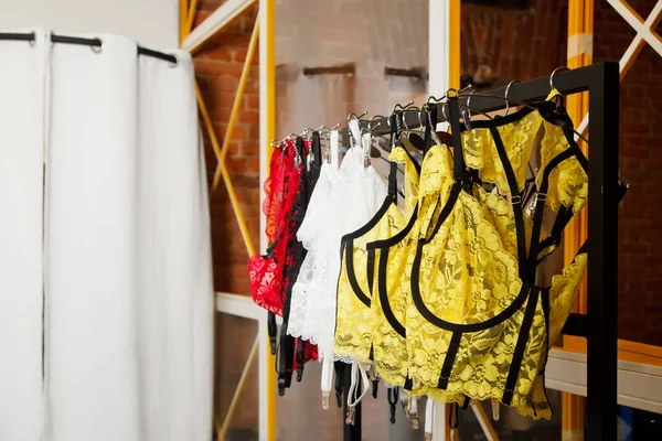 Interior of showroom with underwear clothes. Wardrobe rack with stylish lingerie near brick wall and changing cabin indoors. Details of bright beauty colored wear collection in show room. Copy space