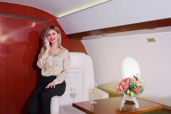 Cute young businesswoman talking on phone flying in luxury private jet. Business woman in airplane first class seat during trip. Concept quality of passenger service in aviation industry, at highest