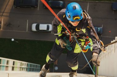 Endüstriyel dağcılık işçisi dış cephe camlarını yıkarken konut binasının ön cephesinde asılı duruyor. İp erişimi olan işçi ev duvarında asılı. Şehir işleri kavramı. Alan için kopyala