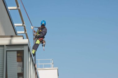 Endüstriyel dağcılık işçisi dış cephe camlarını yıkarken konut binasının ön cephesinde asılı duruyor. İp erişimi olan işçi ev duvarında asılı. Şehir işleri kavramı. Alan için kopyala