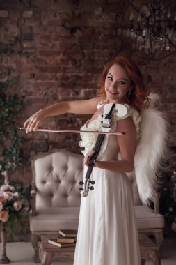 Kemanı ve kanatları olan ince bir kadın. Sahnedeki kadın bir melek. Eski dokulu iç mekanda giyinmiş duygusal kız. Aktris gösterileri. Tiyatro performansı kavramı. Boşluğu kopyala