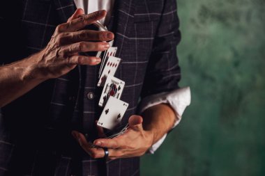 Kumar kartları olan genç bir adamın yakın plan portresi. Yakışıklı adam kartla numara yapıyor. Yeşil dokuda usta sihirbaz elleri. Eğlence ve hobi anlayışı. Alan için kopyala