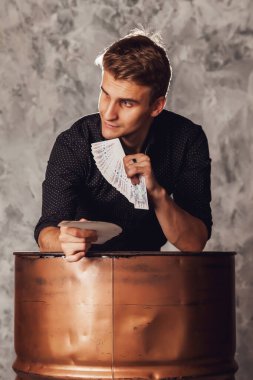 Fıçıdan kumar kartları olan genç bir adamın portresi. Yakışıklı adam kartla numara yapıyor. Gri dokuda usta sihirbaz elleri. Yeraltı kumarı kavramı. Alan için kopyala