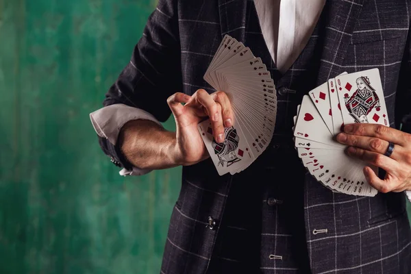 ギャンブルカードを持つ若い男のクローズアップ肖像画 ハンサムな男はトランプでトリックを示しています 緑のテクスチャの背景に魔術師の巧妙な手 エンターテインメントと趣味の概念 サイトのコピースペース — ストック写真