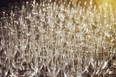 Arka planda bir sürü şarap kadehi var. Barmenin şampanya seremonisi için hazırladığı boş temiz bardaklar mutfağın üzerinde duruyor. Rafta saydam camlar var. Alan için kopyala