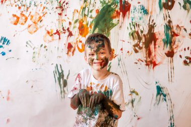 Suluboya ile oynayan mutlu genç bir çocuğun portresi. Çocuk yüzü ve kıyafetleri boyayla boyanmış. Çocuk eğlencesi, sanat oyunları ve holiganlığı kavramsallaştır. Holi festivali için renkli görüntü. Boşluğu kopyala