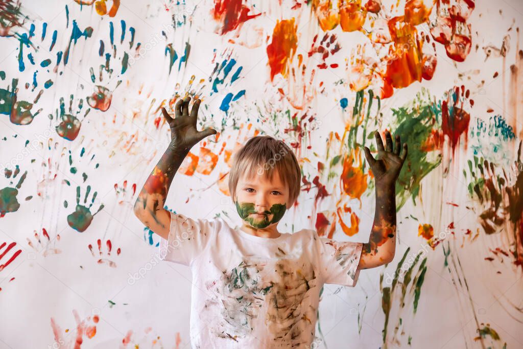 Portrait of happy young child playing with watercolor. Child face and clothes messy painted with paints. Concept children fun, art games and hooliganism. Color image for holi festival. Copy space