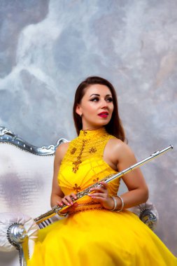 Sahne sarısı elbiseli, elinde flütle genç bir kadın model portresi. Duvarın arka planında flüt çalan rüzgar enstrümanı. Reklam okulu için poster. Konsept müzik ya da konser