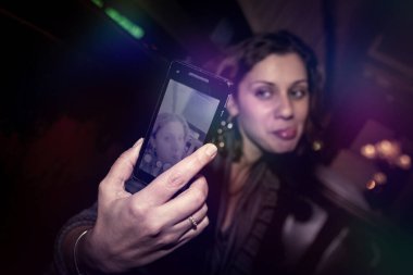 Masadaki gece klübünde pozitif duygusal genç bir kadının sıradan portresi. Kadın telefonda selfie çekiyor ve çok duygulu. Gece hayatı gece hayatı konsepti. Boşluğu kopyala
