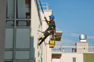 Endüstriyel dağcılık işçisi dış cephe camlarını yıkarken konut binasının ön cephesinde asılı duruyor. İp erişimi olan işçi ev duvarında asılı. Şehir işleri kavramı. Alan için kopyala