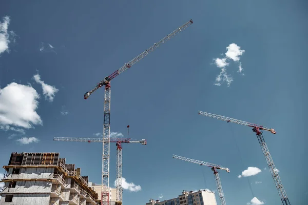 Construction cranes work on creation site against blue sky background. Bottom view of industrial crane. Concept of construction of apartment buildings and renovation of housing. Copy space