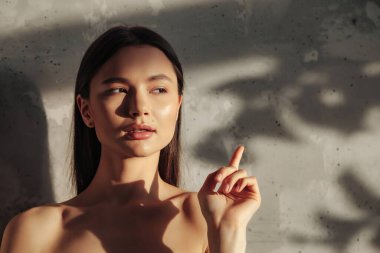 Genç, sevimli, neşeli bir kadının portresi parmaklarını gösteriyor ve duvarın arka planına bakıyor, yaprağın gölgesiyle. Sağlıklı yaşam tarzı ve kişisel bakım reklamları. Alan ya da SPA için kopyala