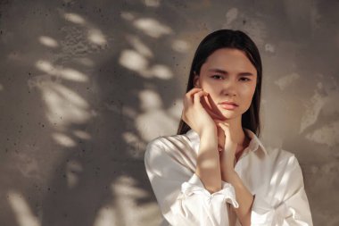 Beyaz tişörtlü, genç ve neşeli bir kadının portresi, yeşillik gölgesiyle duvarın arka planına bakıyor. Sağlıklı yaşam tarzı ve kişisel bakım reklamları. Alan ya da SPA için kopyala