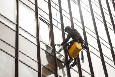 Endüstriyel dağcılık işçisi dış cephe camlarını yıkarken konut binasının ön cephesinde asılı duruyor. İp erişimi olan işçi ev duvarında asılı. Endüstriyel kentsel işler kavramı. Boşluğu kopyala