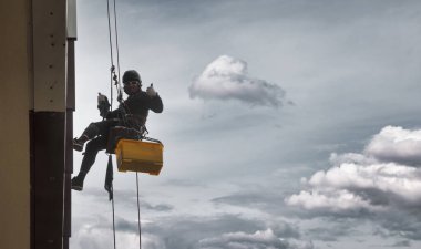 Endüstriyel dağcılık işçisi dış cephe camlarını yıkarken konut binasının ön cephesinde asılı duruyor. İp erişimi olan işçi ev duvarında asılı. Endüstriyel kentsel işler kavramı. Boşluğu kopyala