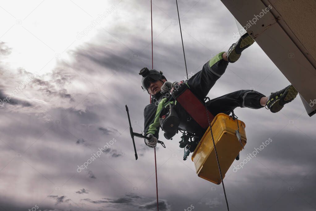 Industrial mountaineering worker hangs over residential facade building while washing exterior facade glazing. Rope access laborer hangs on wall of house. Concept of industry urban works. Copy space