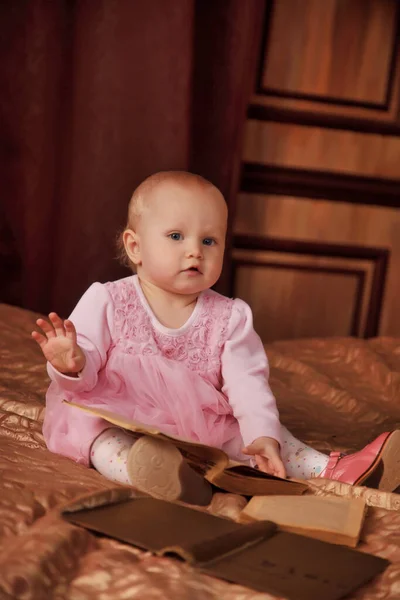 穿着粉色衣服 头戴旧书的漂亮的一岁小女孩正坐在床上的房间里 卧室里的孩子教育和抚养子女的概念 网站或横幅的背景 复制空间 — 图库照片