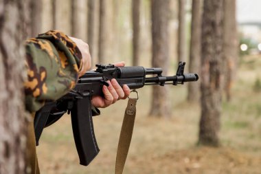 Ormanda, hava yumuşağı ya da grev topuyla oynanan yetişkin savaş takımı oyunları. Askeri kamuflaj üniformalı, gözlüklü, elinde silahı olan bir asker. Orman üniformalı orta yaşlı asker.