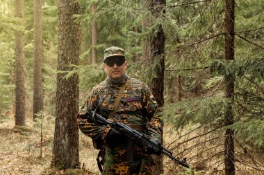 Ormanda, hava yumuşağı ya da grev topuyla oynanan yetişkin savaş takımı oyunları. Askeri kamuflaj üniformalı, gözlüklü, elinde silahı olan bir asker. Orman üniformalı orta yaşlı asker.