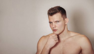 Işık yalıtılmış arka planda atletik yapılı yakışıklı genç bir adamın portresi. Yakışıklı, kaslı, kaslı bir adam. Spor anlayışı, beden eğitimi, fitness ve sağlıklı yaşam tarzı. Boşluğu kopyala