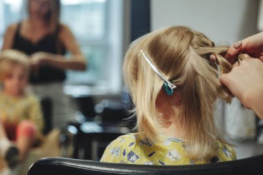 Berber kadın, modern berber dükkanında, kuaförde küçük sevimli sarışın kız çocuğu için şık bir saç stili yapıyor. Berber dükkanında kuaför, küçük bebek için kuaför yapar. Saç stili ve güzellik kavramı