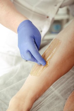 Özenli kozmetik uzmanı spa salonunda çalışıyor. Deri bacağına özel balmumu malzemesi uyguluyor. Kadın bacaklarında tüy dökülmesine yakın çekim. Sağlıklı yaşam tarzı ve bakımlı cilt anlayışı