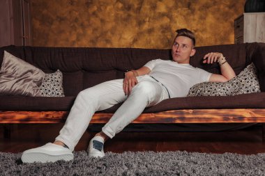 Beyaz giysili müthiş ilgisiz genç adam evdeki oturma odasının içindeki kanepede uzanıyor. Tembel bakışlı, sandalyedeki yakışıklı erkek. Sıkıntı ve depresyon kavramı. Alan için kopyala