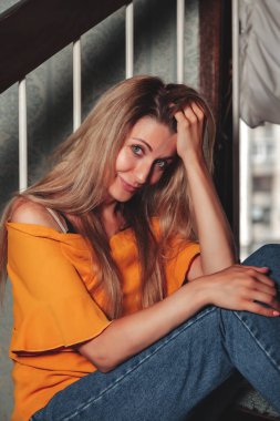 Ev merdivenlerinde poz veren yetişkin kadın aktris klasik oturma odasında stil giysiler giyiyordu. Uzun saçlı, turuncu ceketli bir kadın. Eski moda ve modası geçmiş moda kavramını benimse