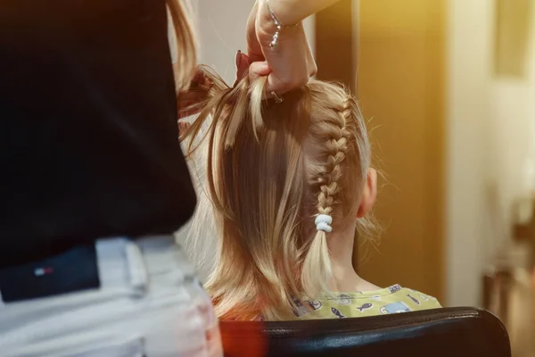 Barber woman make fashionable pretty hairstyle for cute little blond girl child in modern barbershop, hair salon. Hairdresser makes hairdo for young baby in barber shop. Concept hairstyle and beauty