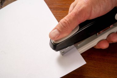 Bir adam zımbayla birkaç sayfa kağıt zımbalıyor.