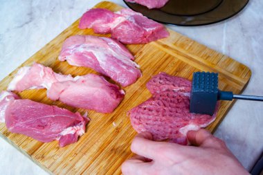 Bir kadın et kıran bir çekiçle et doğrayan bir tahtada çiğ domuz eti doğruyor.