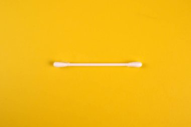 one cotton swabs lies on a yellowe background.
