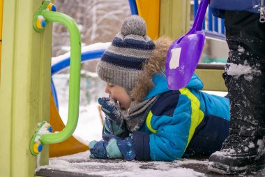 a little boy eats snow from a mitt in winter