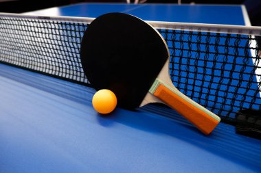 Tenis masasında bir top ve iki masa tenisi raketi var.