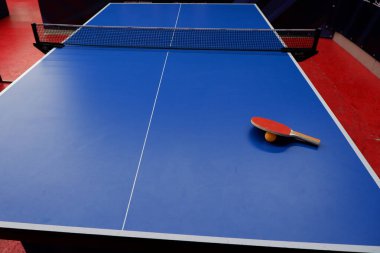 Tenis masasında bir top ve iki masa tenisi raketi var.