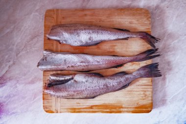 Kesme tahtasının üzerinde çiğ pollock balığı leşleri var.