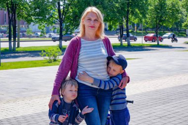 Şehir sokaklarında güneşli bir havada iki oğlu olan güzel bir kadının portresi..