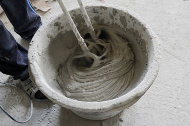 İnşaatçı, çözeltiyi mikserle karıştırmak için yapı karışımını bir kabın içinde karıştırır.,