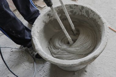İnşaatçı, çözeltiyi mikserle karıştırmak için yapı karışımını bir kabın içinde karıştırır.,