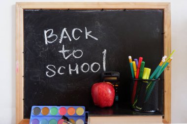 Okul malzemelerinin arasında karatahtaya yazılan yazı.