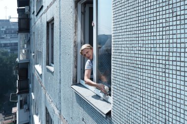 Bir kadın dışarıdaki yüksek katlı bir binanın camını temizliyor.,