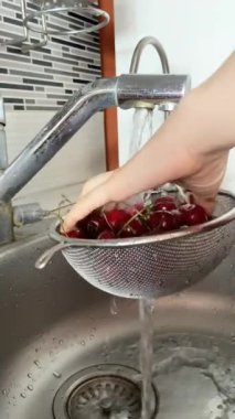 Womans hands washing cherries in a sieve in the kitchen in the sink