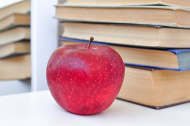 Okul masasında eski kalın ders kitabı ve kırmızı elma, bilgi konsepti, sıkı çalışma