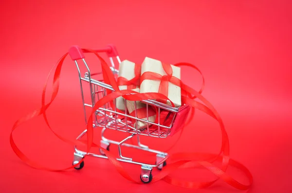 Geschenk in Packpapier im Warenkorb auf rotem Hintergrund Urlaub Verkauf — Stockfoto