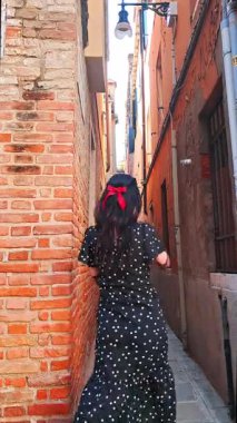 Genç esmer turist Venedik sokaklarında tek başına geziyor. Esmer gezgin, Venedik kanallarını keşfediyor. Zarif yaz elbisesiyle kırmızı kurdeleli.