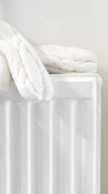 Sıcak bir el beyaz bir radyatöre dokunuyor, ev ısıtmasını ve kışlık konforu gösteriyor..